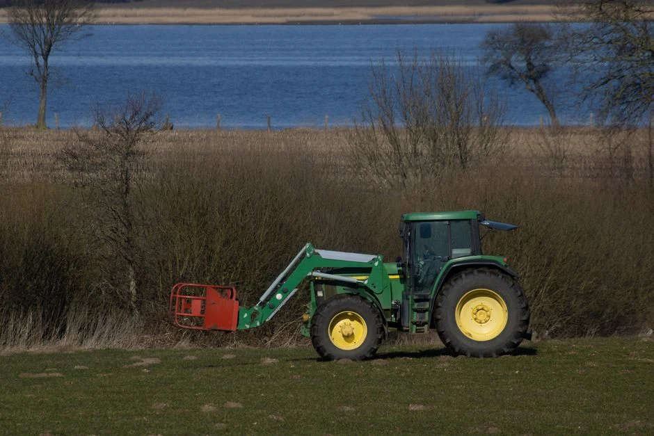 A green tractor parked in a picturesque rural area near water with bushes and a field