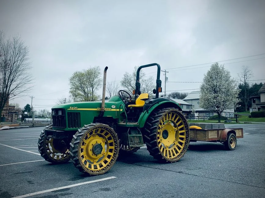A green tractor with yellow wheels parked outdoors on a cloudy day in Lancaster, PA