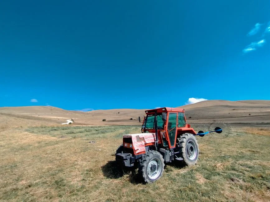 A red tractor sits on a grassy field with clear blue skies and rolling hills