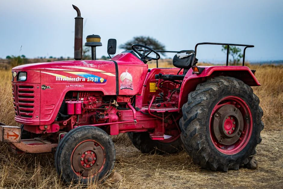 A vivid red tractor sitting idle in a dry, barren field under an overcast sky