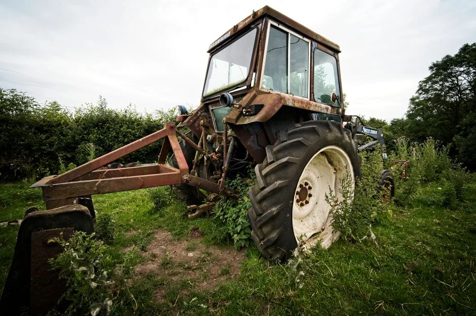 An old, rusted tractor overgrown with weeds in the English countryside