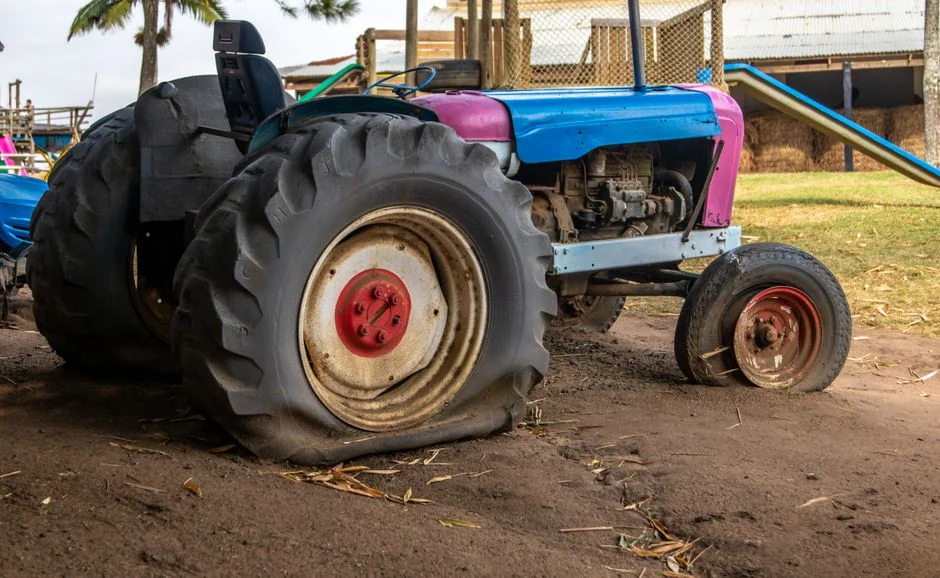 An old vintage tractor with flat tires parked on a rural farm setting