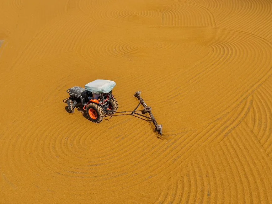 A solitary tractor creating intricate patterns in a vast yellow field from high above