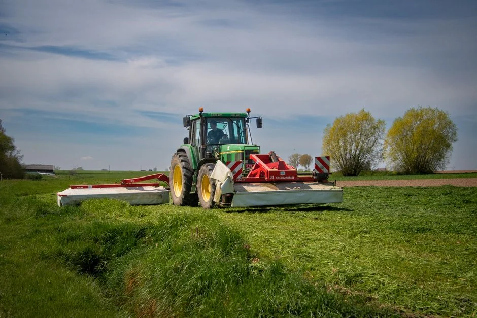 Tractor Tire Types Explained: R1 vs R2 vs R3 vs R4 A green tractor mows a grass field on a sunny day, showcasing modern farming equipment