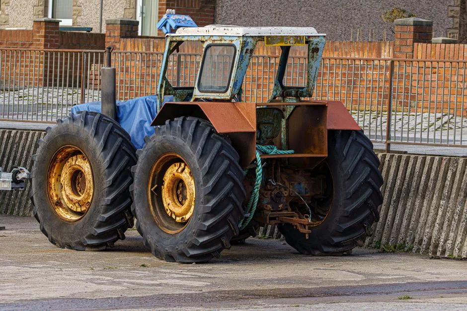 A rusted vintage tractor parked against a brick wall in the UK