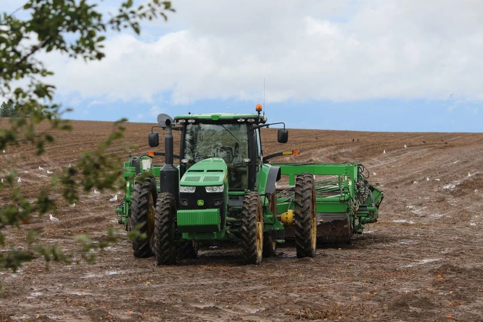 A large green tractor working on a plowed field