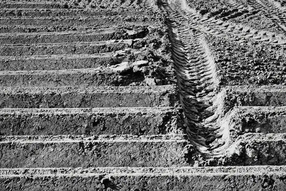Monochrome image of a plowed field with distinct tractor tire marks and soil texture