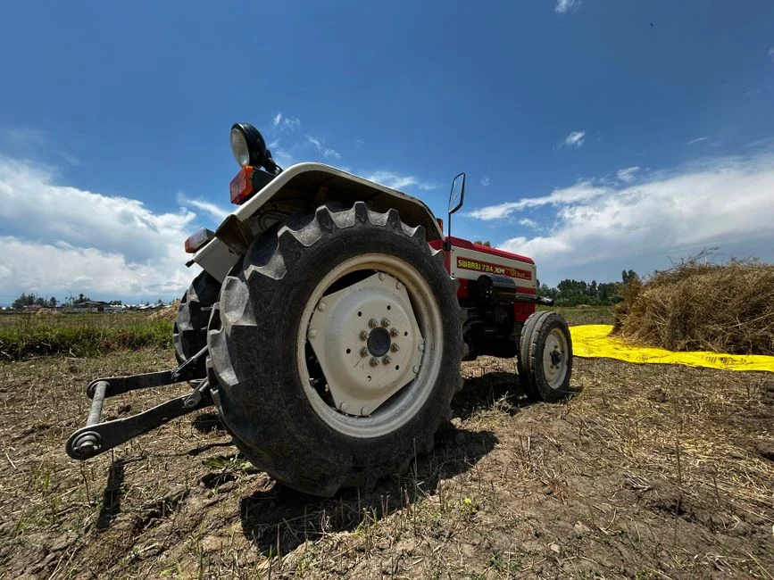 Tractor Tire Types Explained: R1 vs R2 vs R3 vs R4 A red tractor sits in a field under a clear blue sky, surrounded by farmland scenery
