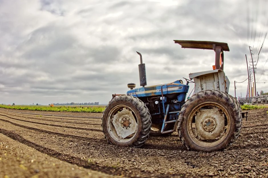 Tractor Tire Types Explained: R1 vs R2 vs R3 vs R4 A vintage blue tractor sits idle on freshly plowed farmland under a cloudy sky