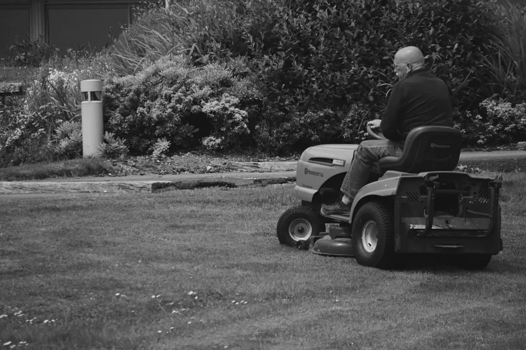 Adult mowing grass on a ride-on lawn mower in a garden