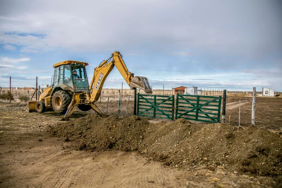 Backhoe loader digging soil at a farm entrance