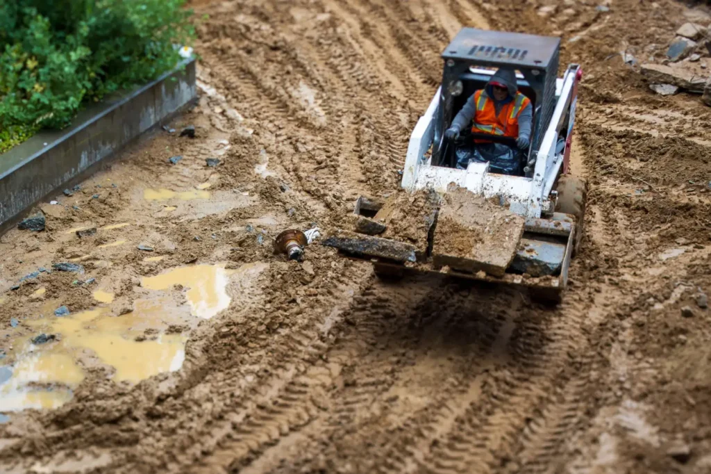 Worker operating a backhoe on a muddy construction site