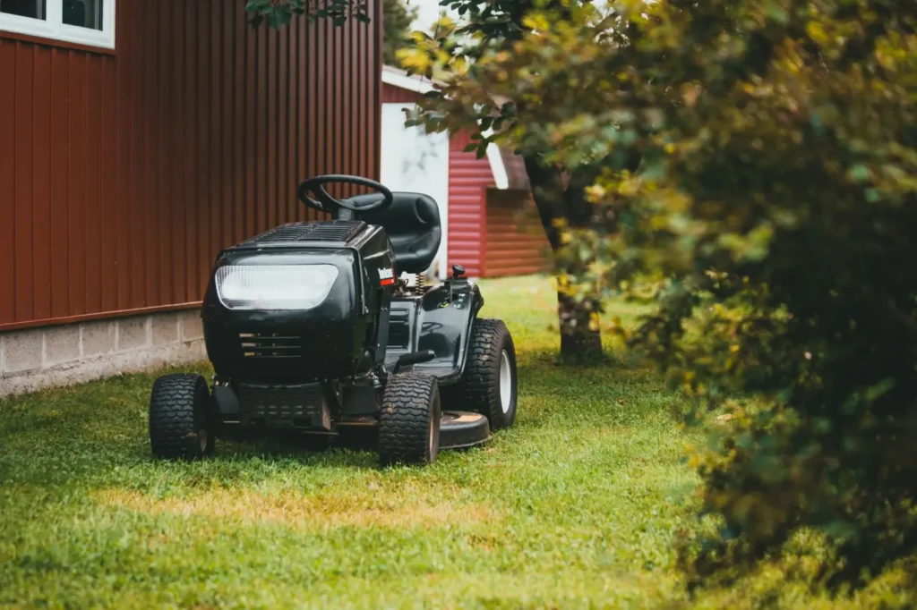 Black ride-on lawn mower parked on green grass near a red barn