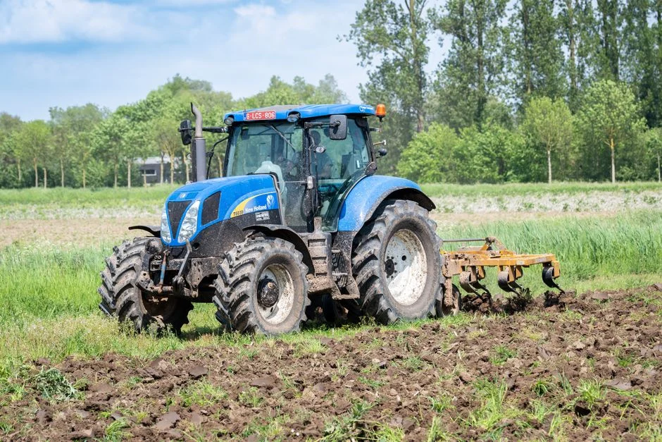 Blue tractor with big rear tires cultivating a green field