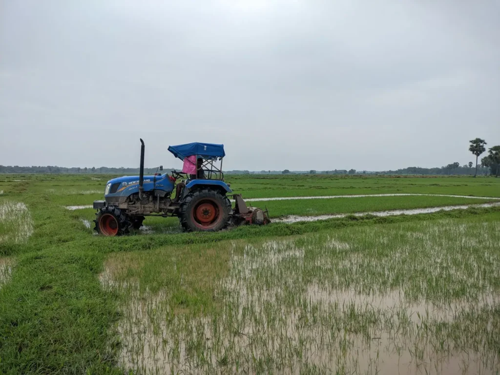 Blue tractor plowing a rice field on an overcast day
