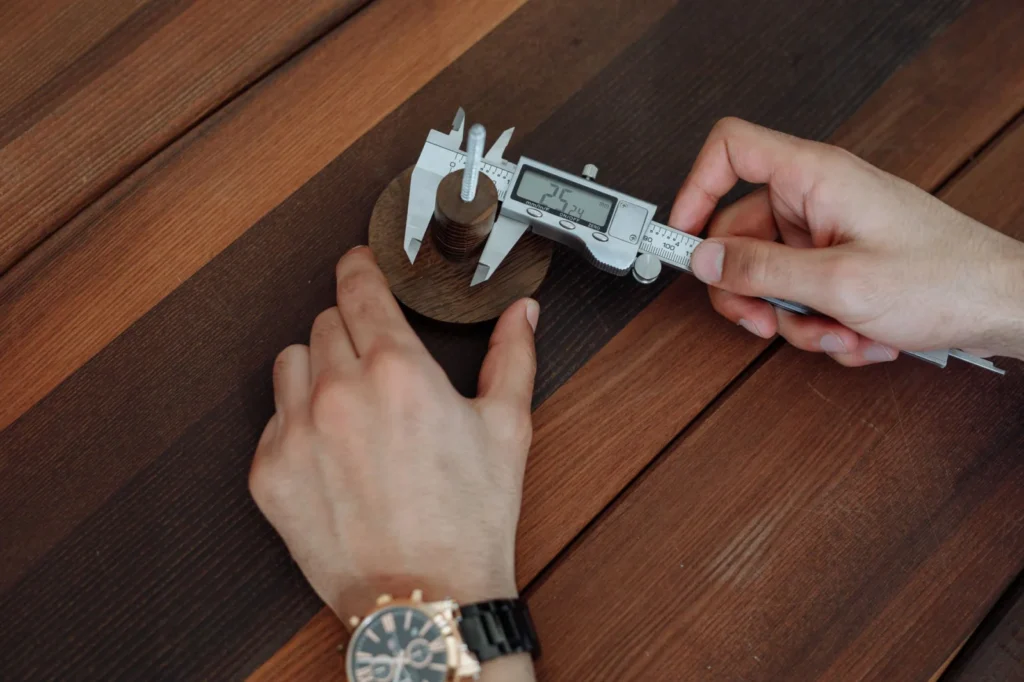 Hands using a digital caliper to take a measurement on a wooden table