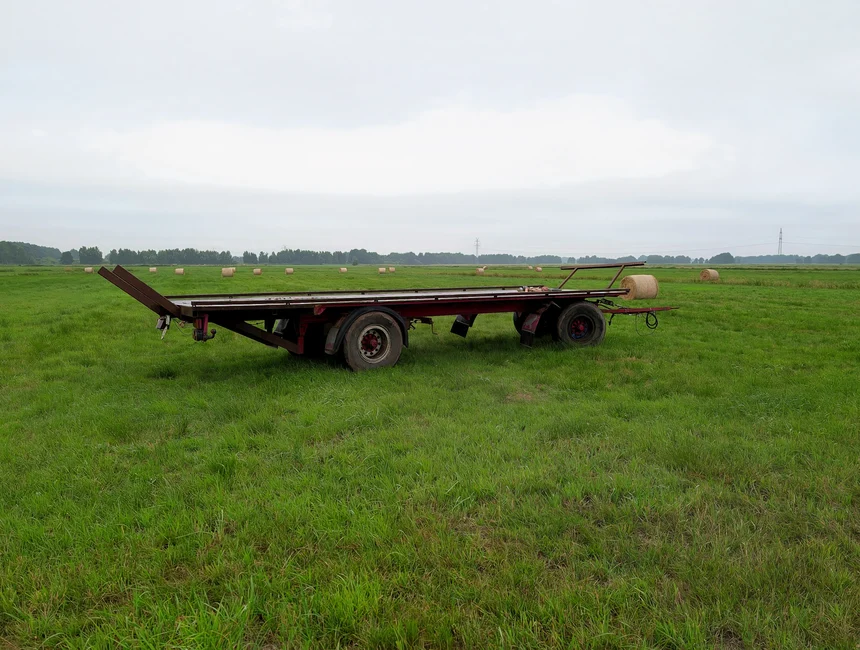 An empty hay trailer on a green field under a cloudy sky, showcasing a tranquil rural scene.