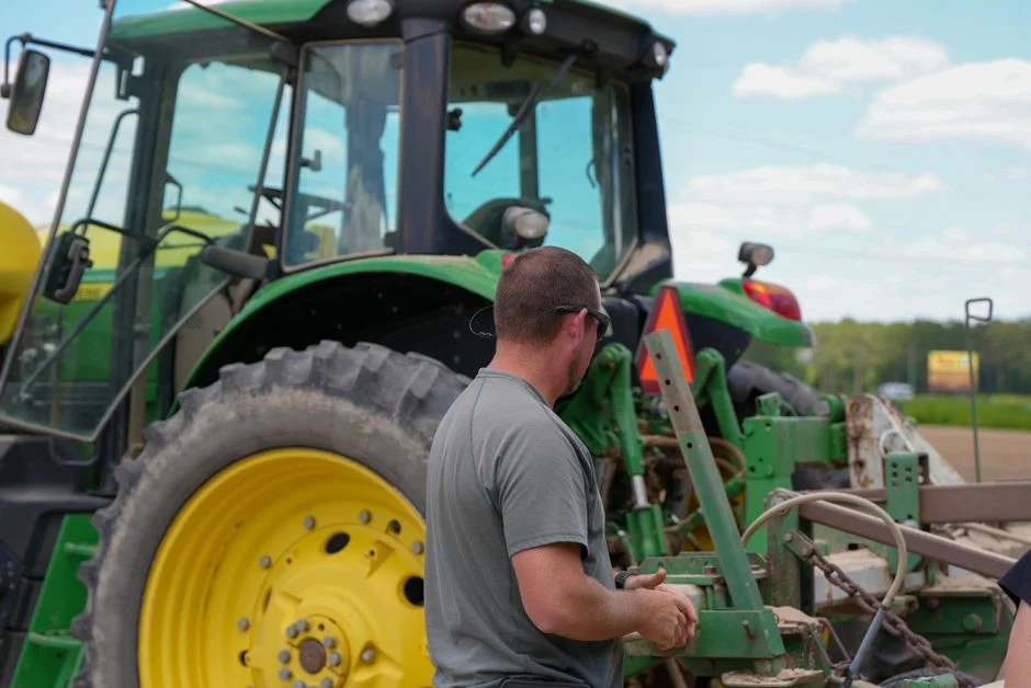 Man examines large green tractor in a sunny rural field