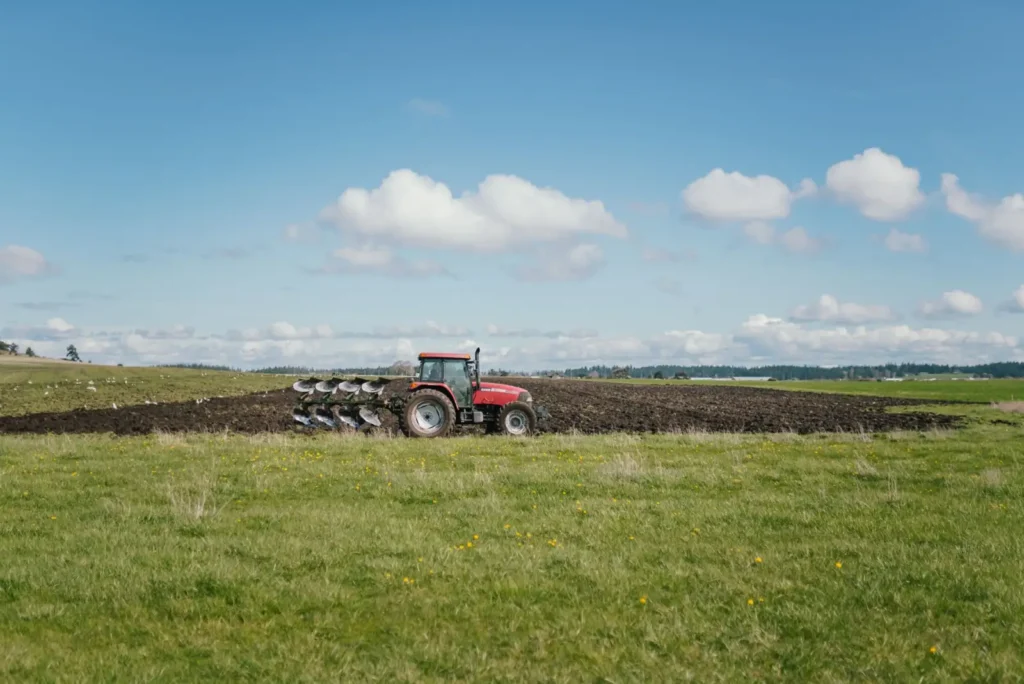 Red tractor plowing fertile farmland under a clear blue sky