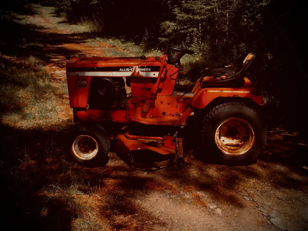 Classic red lawn tractor parked on a dirt road surrounded by trees