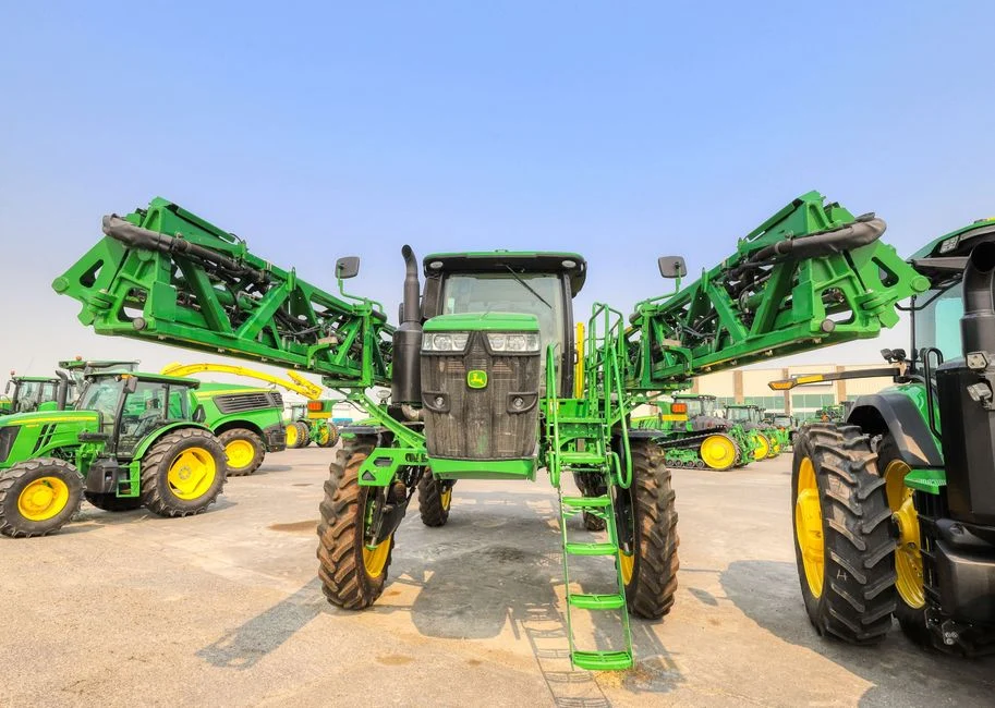 Green tractor with large wheels parked outdoors under a blue sky