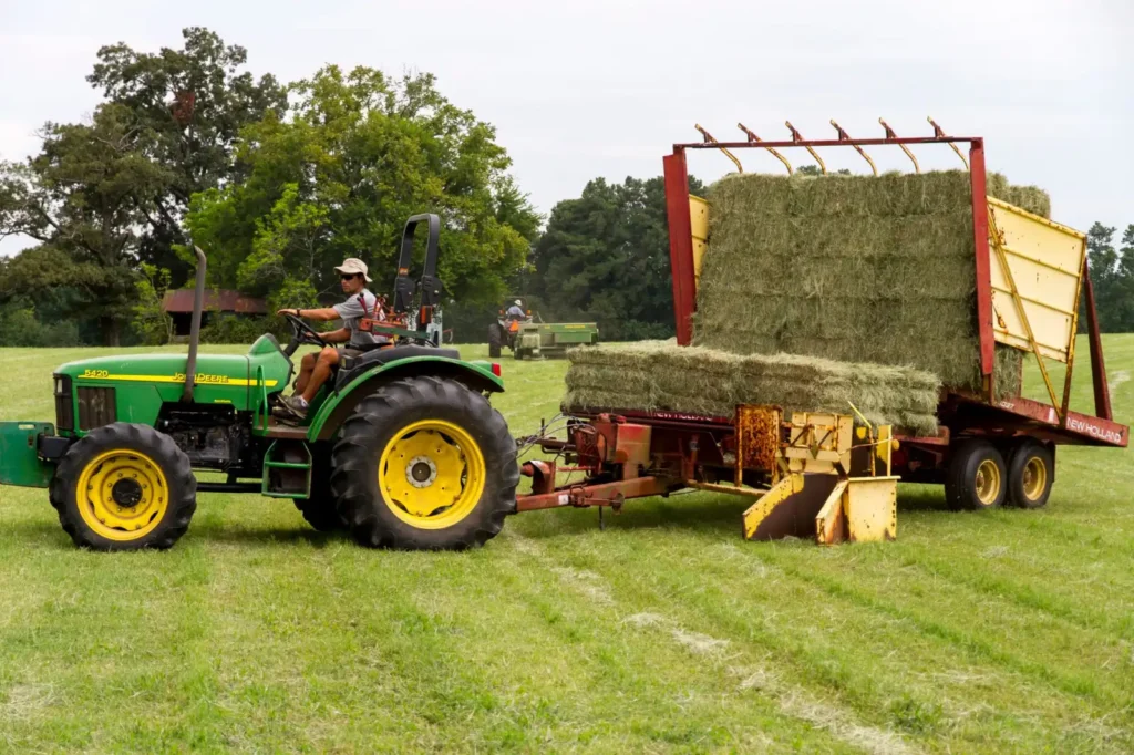 Green tractor with a front loader moving hay in a field