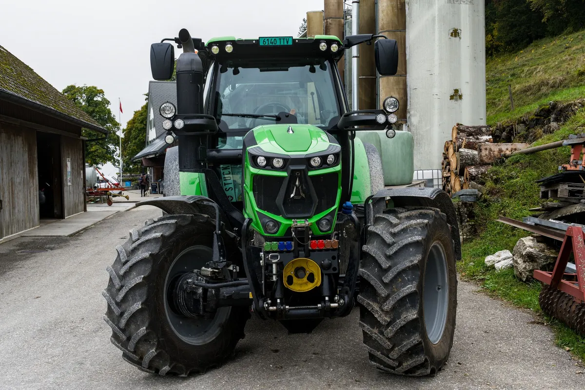 Front Tractor Tires: Which Tread, Size and Pair to Buy Green tractor positioned on a rural farm road surrounded by farm buildings and equipment.