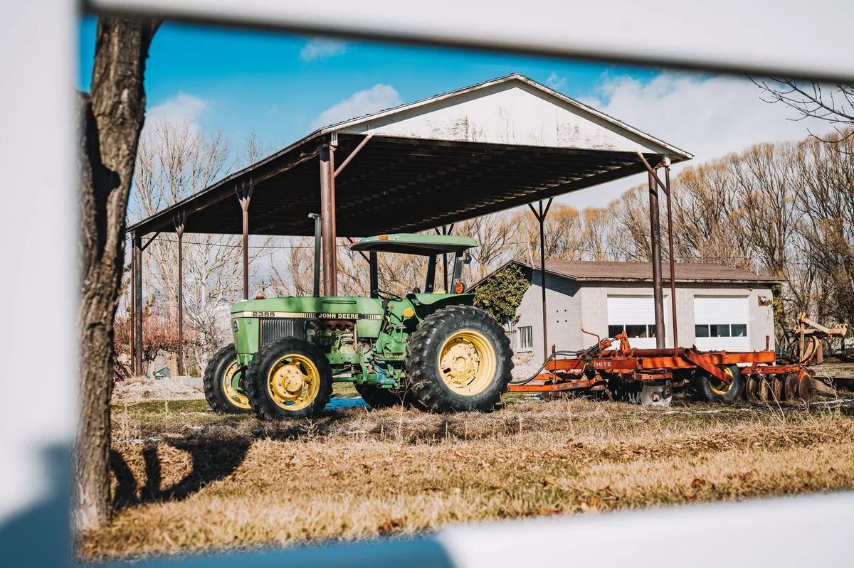 A green tractor parked under a shed on a sunny rural farm day.