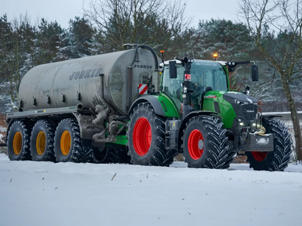 Green tractor towing a tank through a snowy field