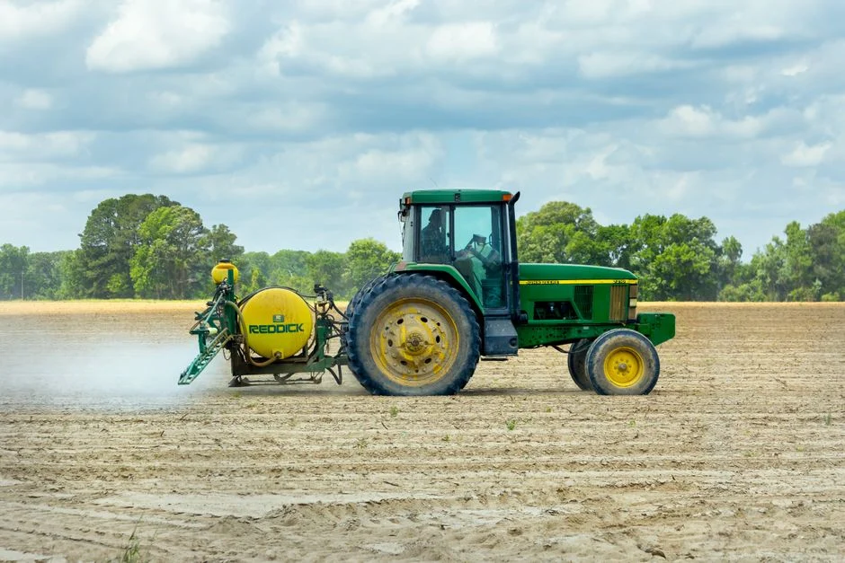 Green tractor with a sprayer working an open farm field