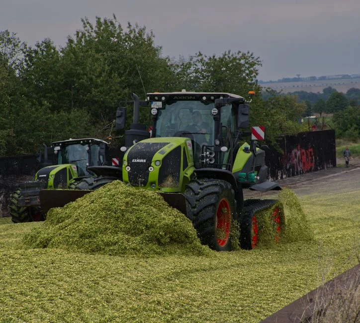 Big Tractor Tires: How Big They Get, What They Fit and Cost A modern CLAAS tractor heaping silage in an open field with a rural backdrop