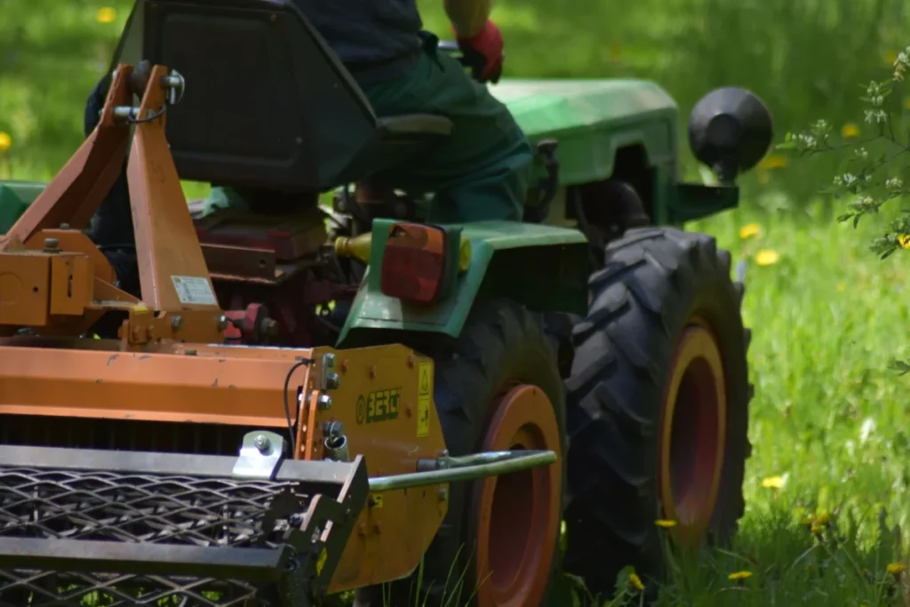 Rear view of a person using a tractor mower in a green field in summer