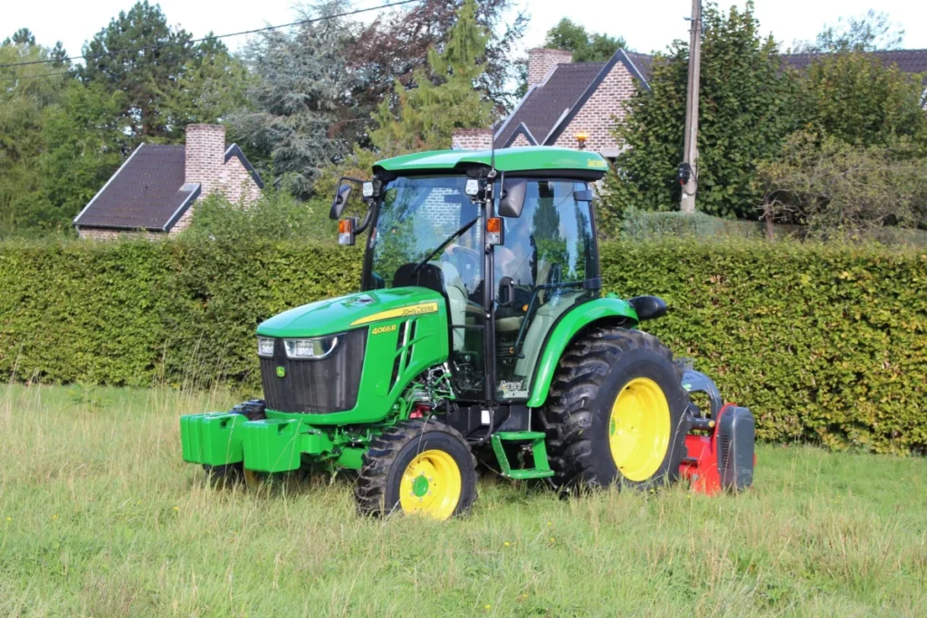 Green tractor mowing grass in a countryside setting with houses and trees