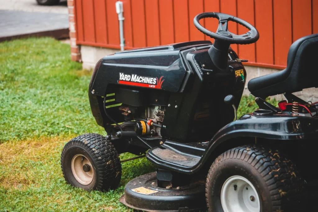 Black riding lawn mower parked on a lawn next to a red building