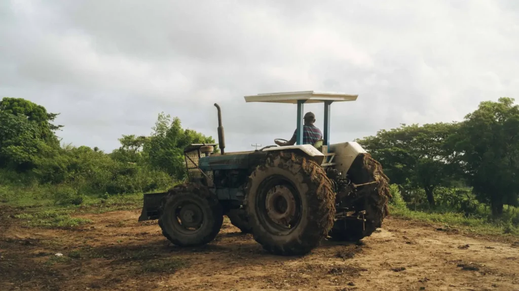 Tires for Compact Tractors: R1, R3 or R4 Tread? Man driving a tractor across a farm field with green plants around