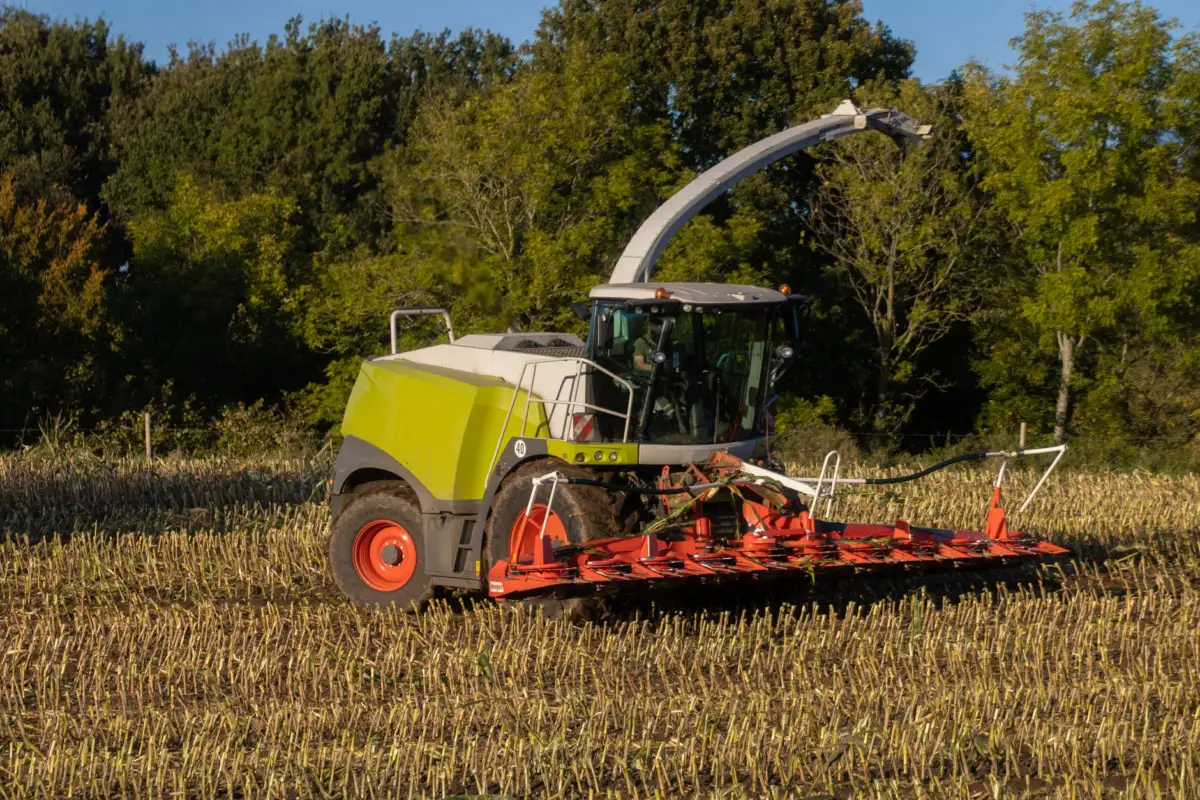 Rear Tractor Tires: Sizes, Tread and How to Pick a Pair A modern tractor plowing a cornfield in the countryside with green trees in the background.