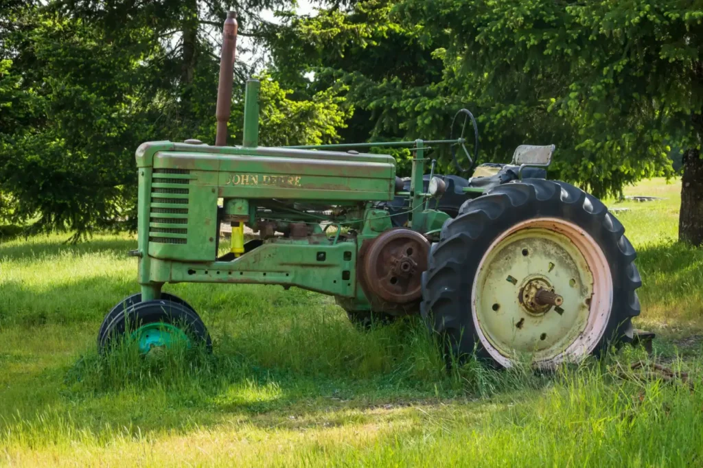 Tires for Compact Tractors: R1, R3 or R4 Tread? Old green tractor standing on a grassy field with trees around it