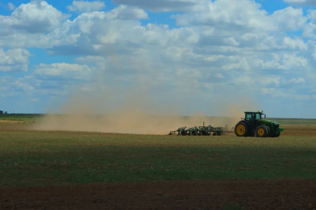 Tractor working a dusty field under a blue sky with clouds