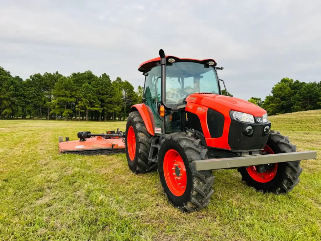 Red tractor with a mower attachment cutting grass in a green field with trees behind