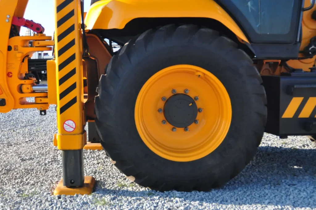 Close-up of a backhoe tire and stabilizer leg resting on gravel at a worksite