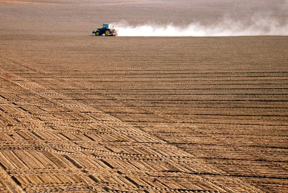 A tractor plowing through a vast, freshly tilled agricultural field during the day