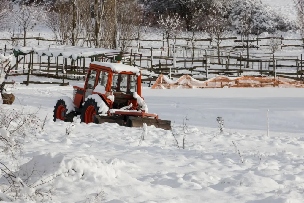 Red tractor covered in snow on a winter farm with fences and trees
