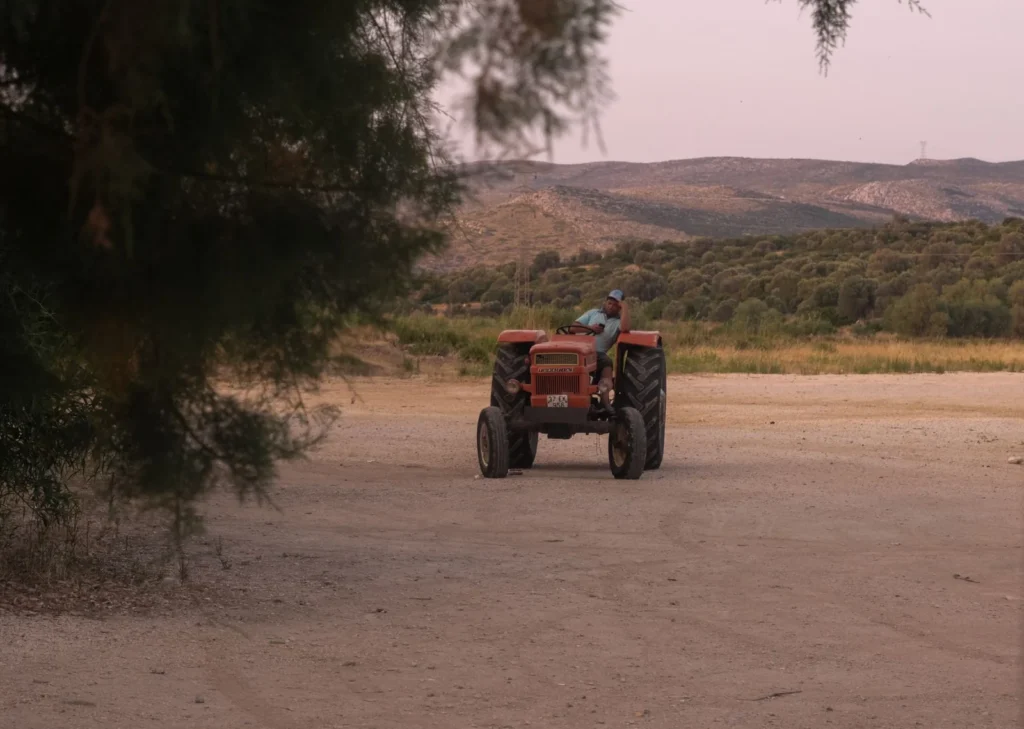 Farmer driving a red tractor on a dusty path with hills behind