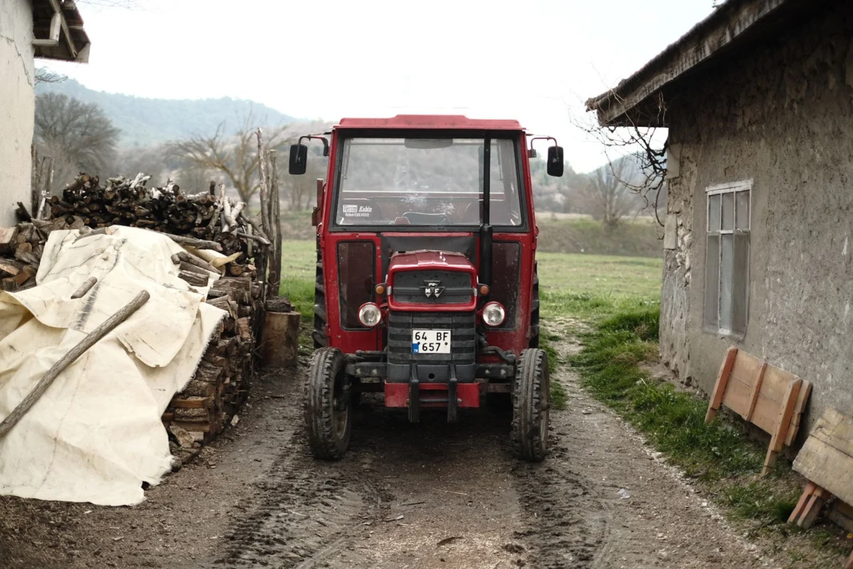 Firestone Tractor Tire Size Chart: Every Size by Model A red tractor parked on a rural farm road beside wooden logs and a stone house.