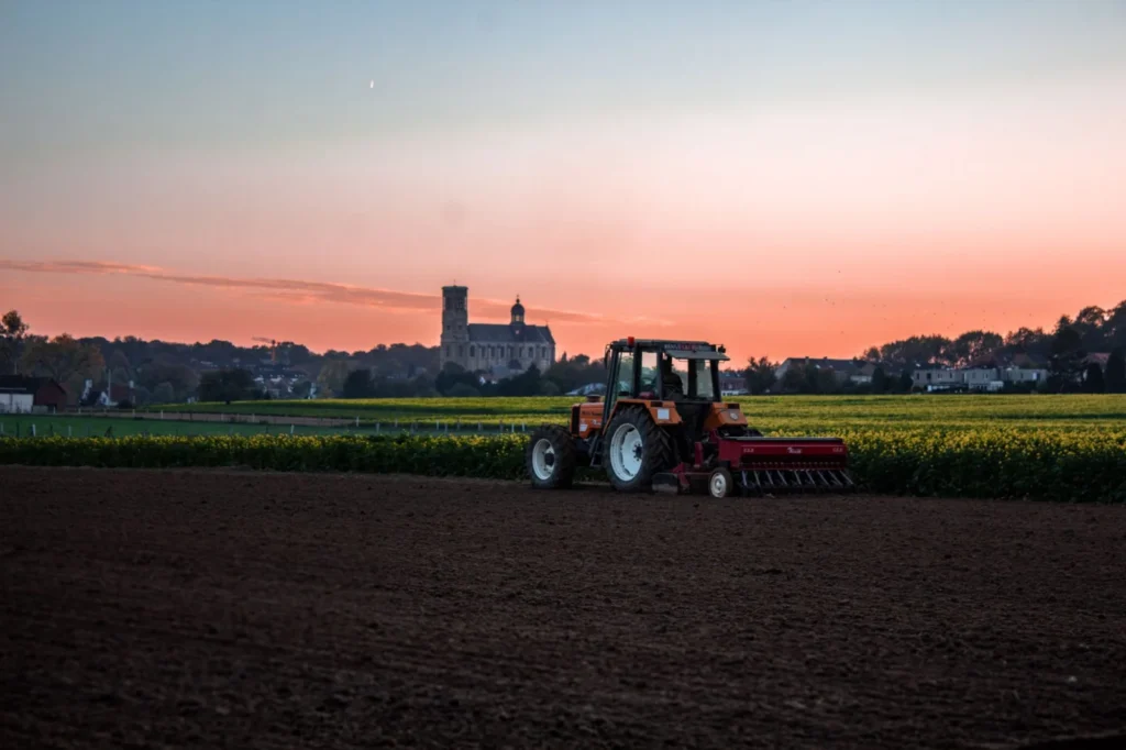 Trelleborg Tires: Who Owns Them, What They Make and Sizes We List A red tractor plows a field under a vibrant sunset near a countryside landmark.