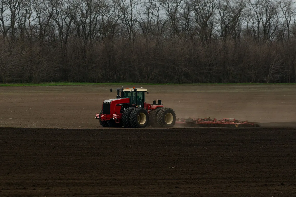 Red tractor plowing a vast field in the countryside, preparing for planting season.