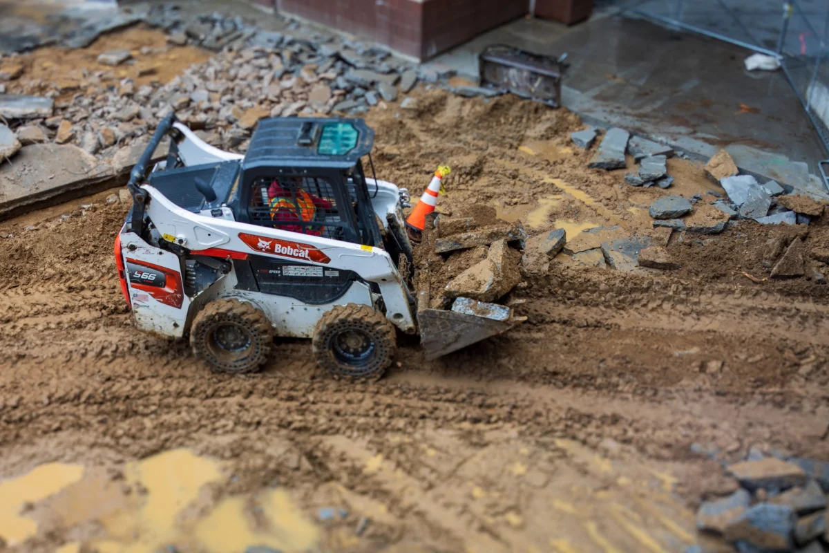 A skid steer loader moves rocks on a muddy construction site, showcasing construction machinery in action.