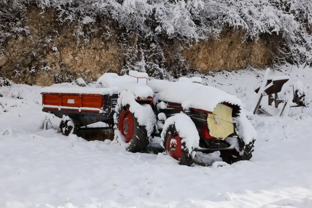 Snow-covered vintage tractor resting on a winter farm