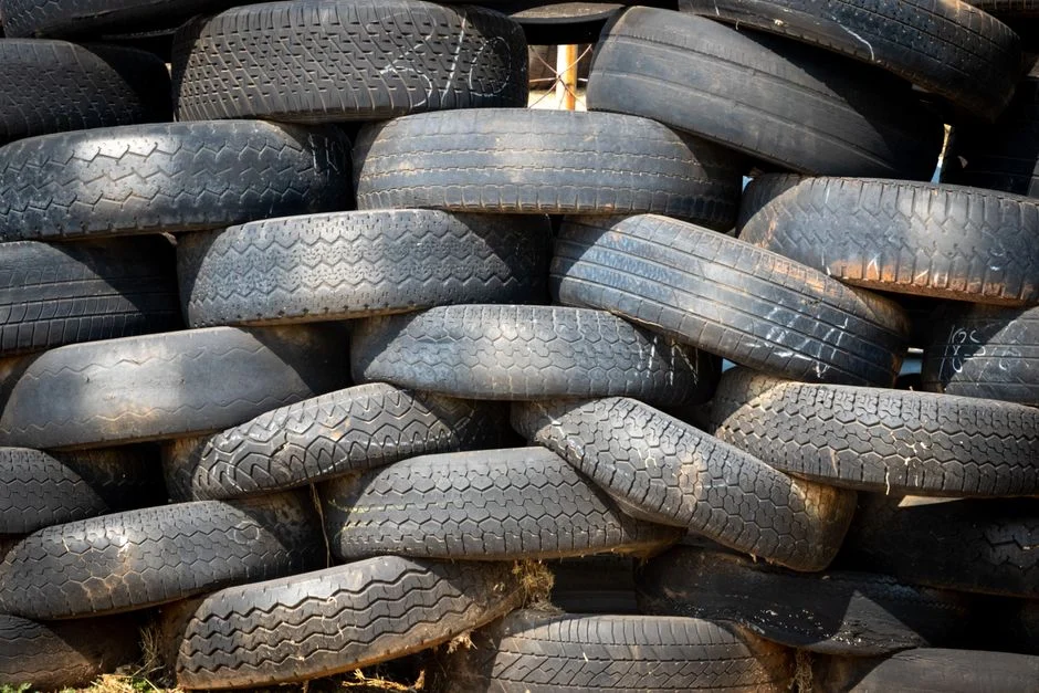 Pile of black rubber tires stacked outdoors in daylight