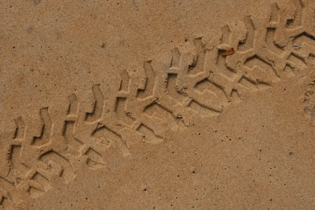 Close-up of tire tracks indented in sandy ground, showcasing pattern and texture.